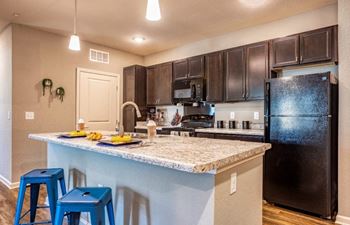 Kitchen with a large island and black refrigerator at Flats at Sundown apartments
